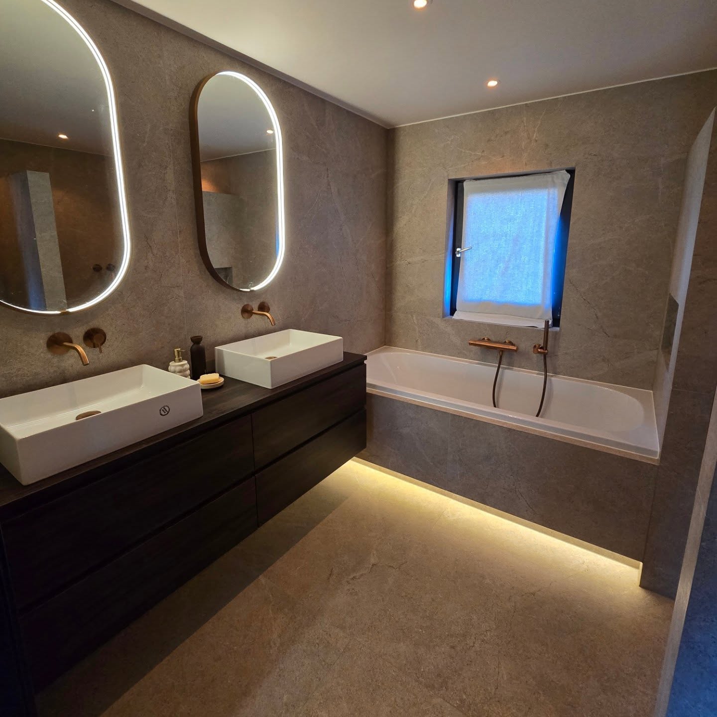 Gerenoveerde badkamer met verlichte spiegels, dubbele wastafels en een ingebouwd bad